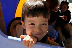Young boy sitting in a playground structure smiling into the camera